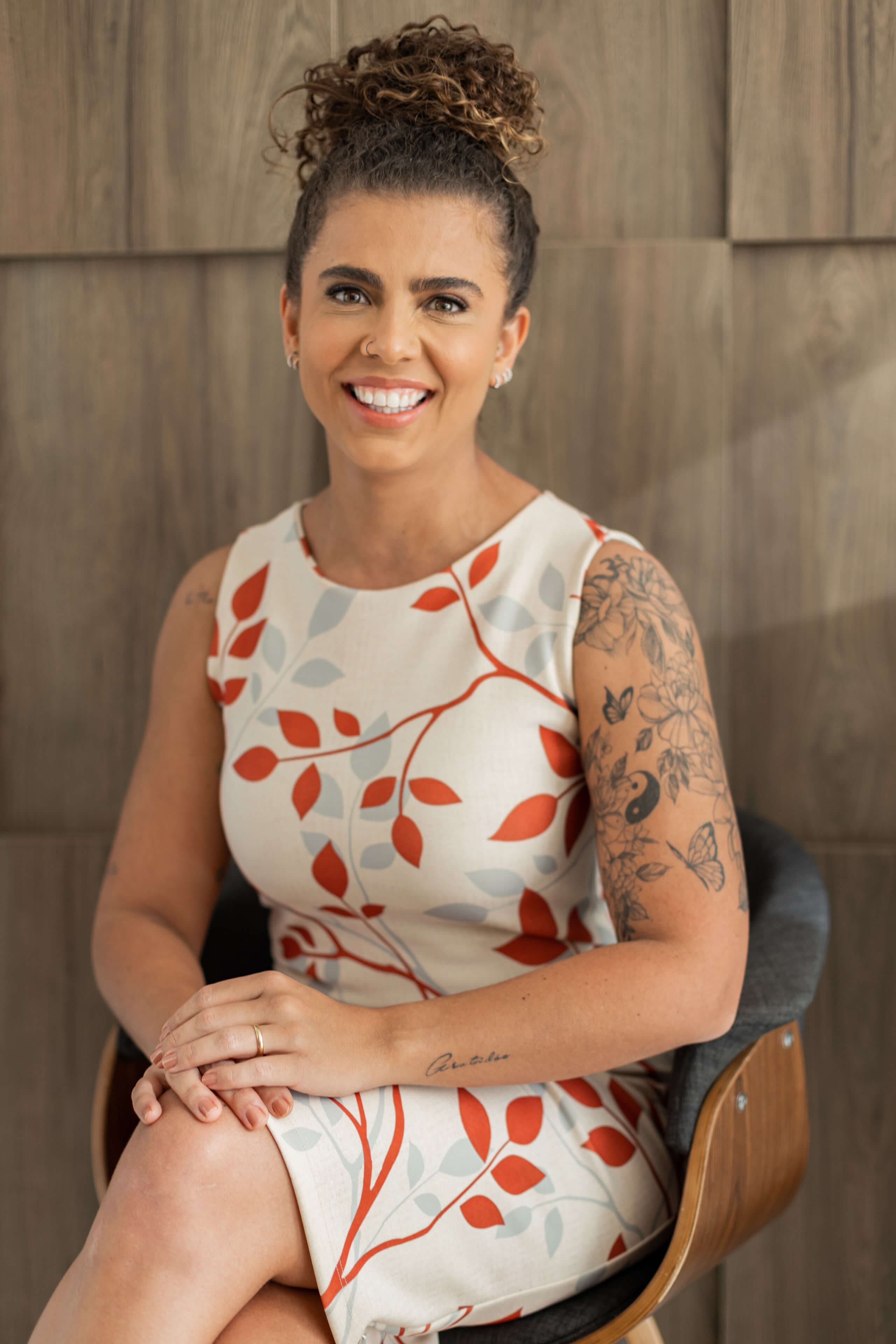 Foto profissional da Dra. Naiara galvão, sentada de frente para uma mesa, com os braços cruzados e com um computador branco a sua frente, exibindo um largo sorriso caloroso.